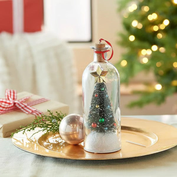 Christmas tree in a corked glass bottle on a gold tray beside a wrapped gift