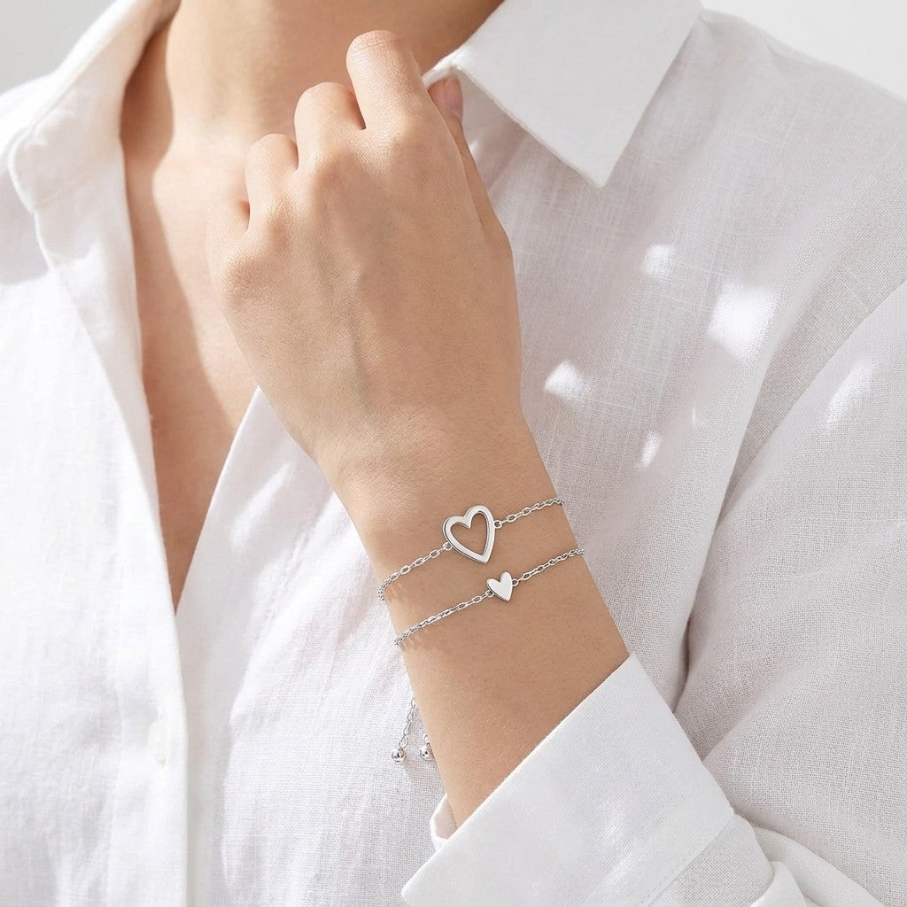 Silver open-heart and solid-heart bracelets stacked on a wrist with a white linen shirt
