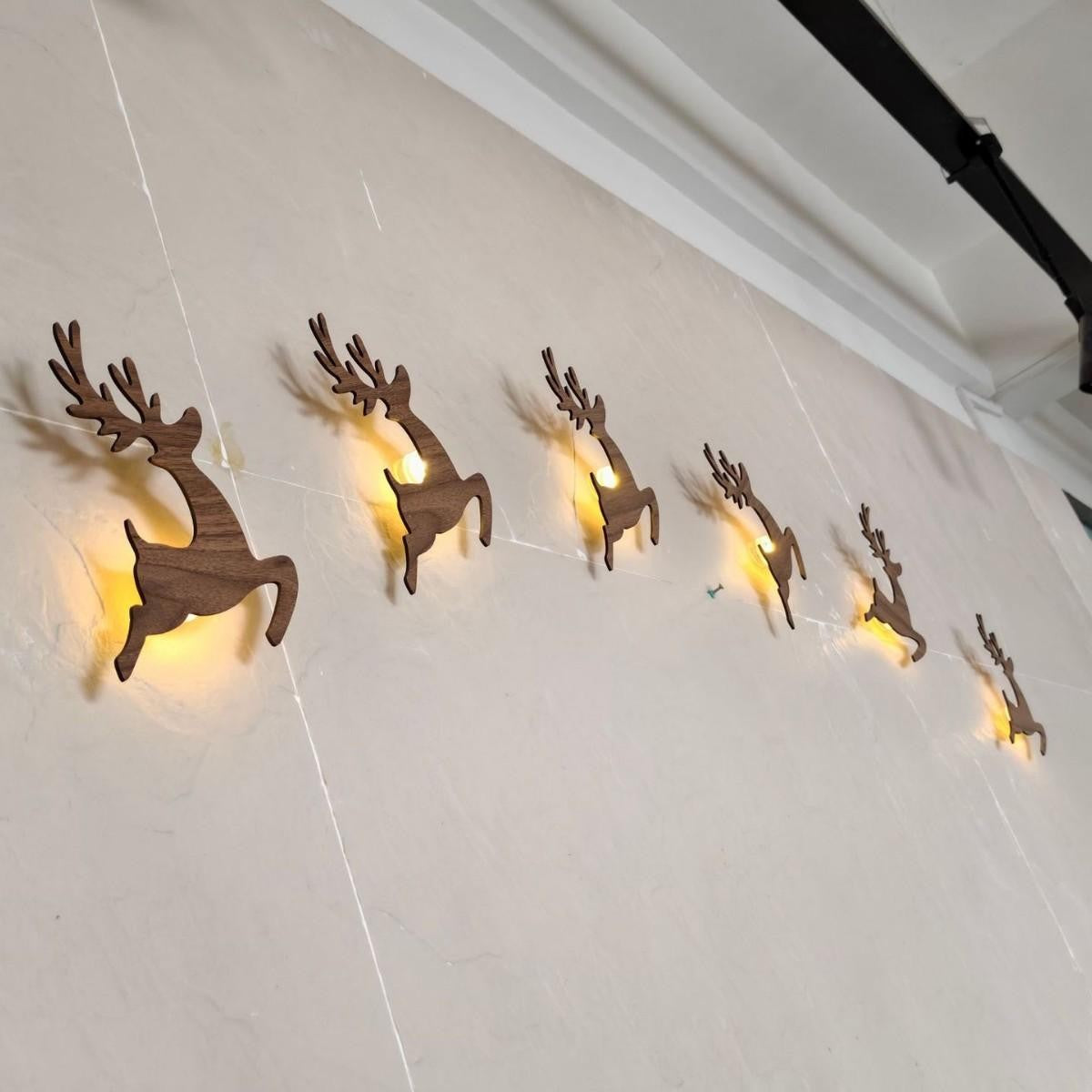 Wooden reindeer silhouettes mounted along a wall with warm light glowing behind each one